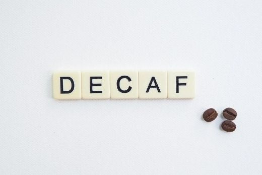 Spielsteine bilden das Wort DECAF neben entkoffeinierten und bereits gerösteten Kaffeebohnen