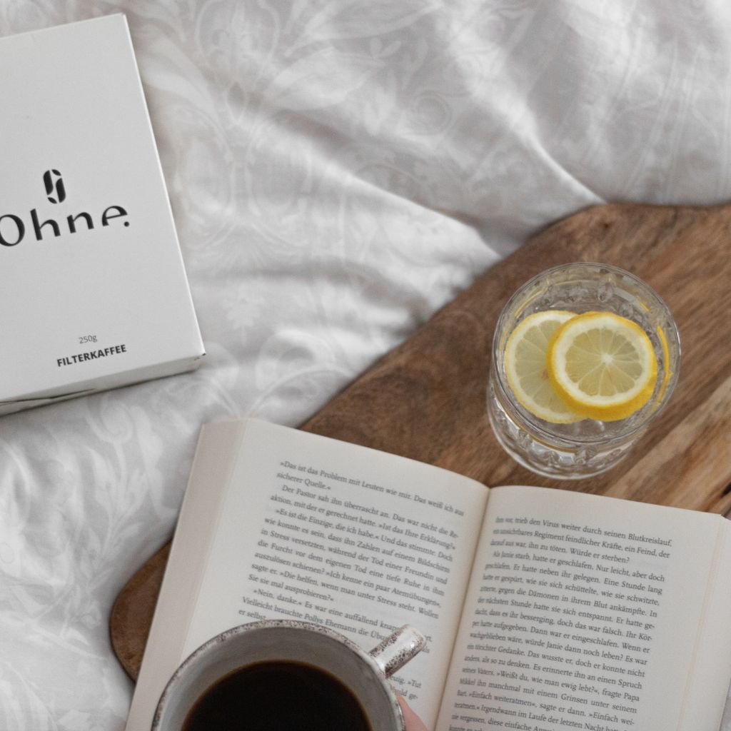 Entkoffeinierter Filter Kaffee von OHNE auf dem Bett neben einer Kaffee Tasse und einem Buch zur Entspannung