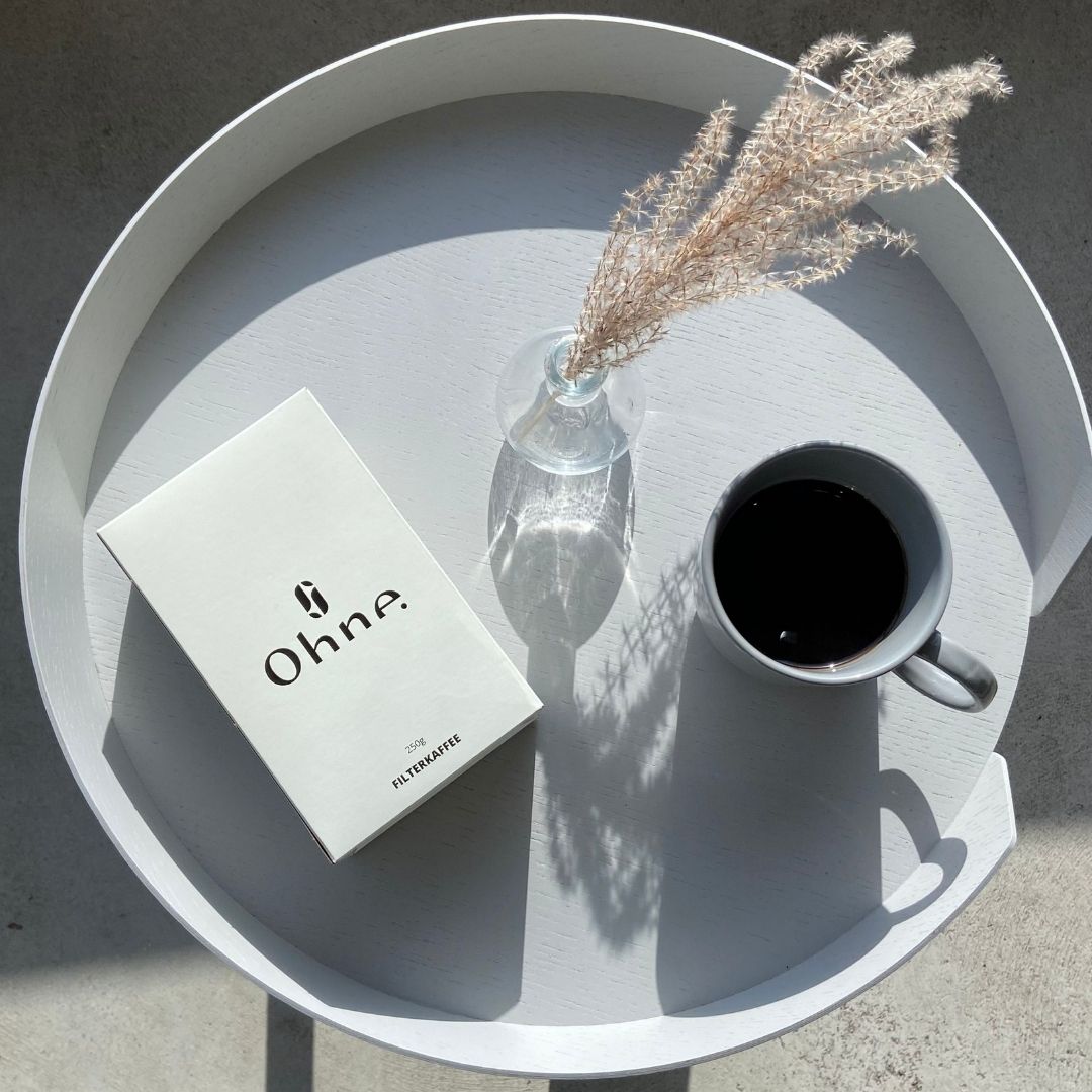 Entkoffeinierter Filterkaffee von OHNE steht auf einem stylischen Tisch neben einer Tasse frisch gebrühtem Kaffee